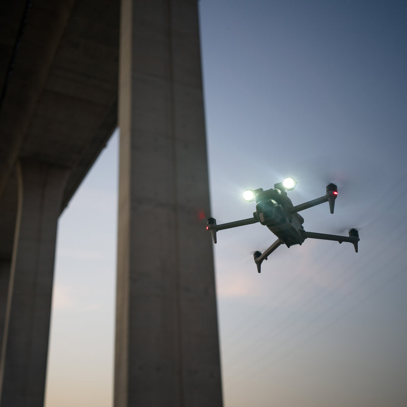 A DJI Matrice 4E drone with the AS1 Spotlight performing bridge inspections at dusk