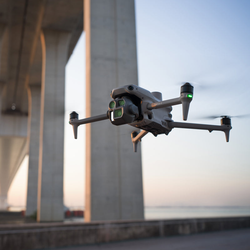 A DJI Matrice 4E drone flying under a bridge