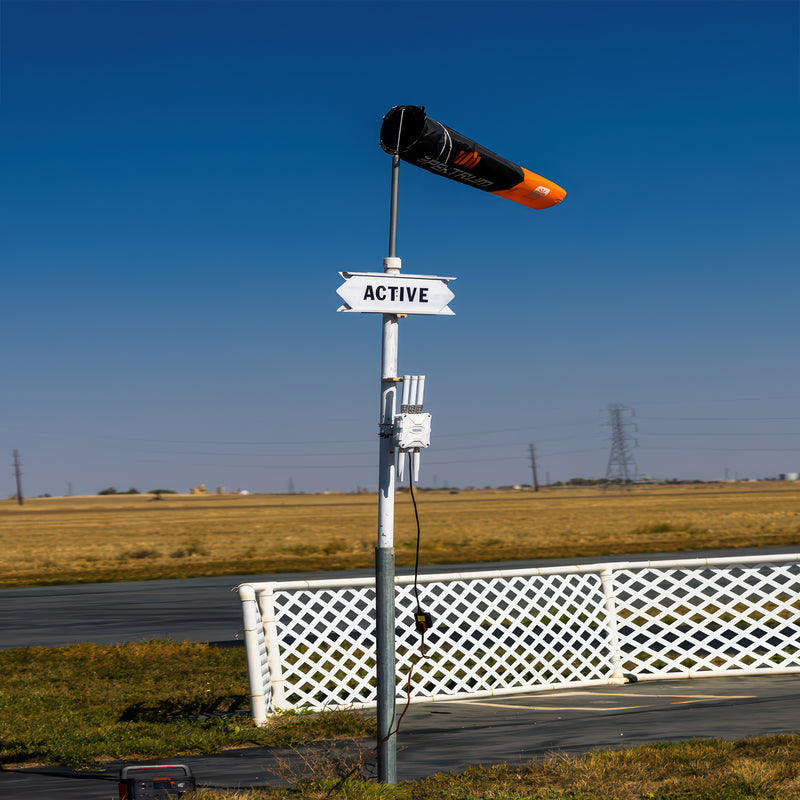 A UAS Sentry Drone RID Detection Unit mounted on a pole near an airfield with a wind sock